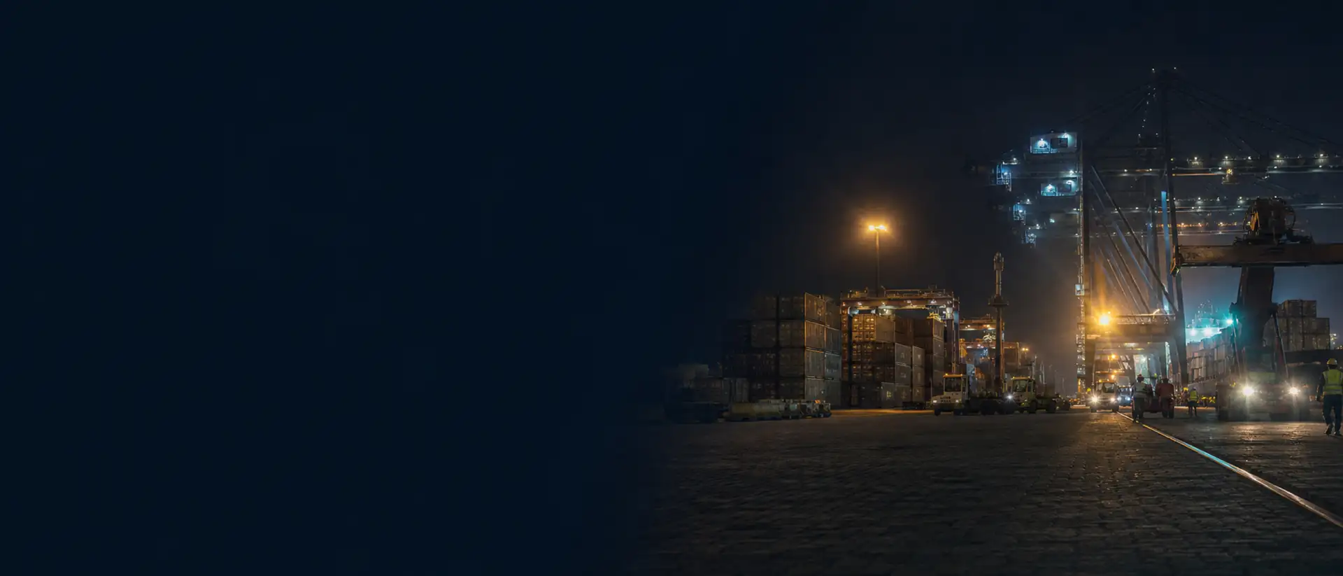 Terminal de contenedores de noche: grúas y muelle iluminados sobre el patio en penumbra.